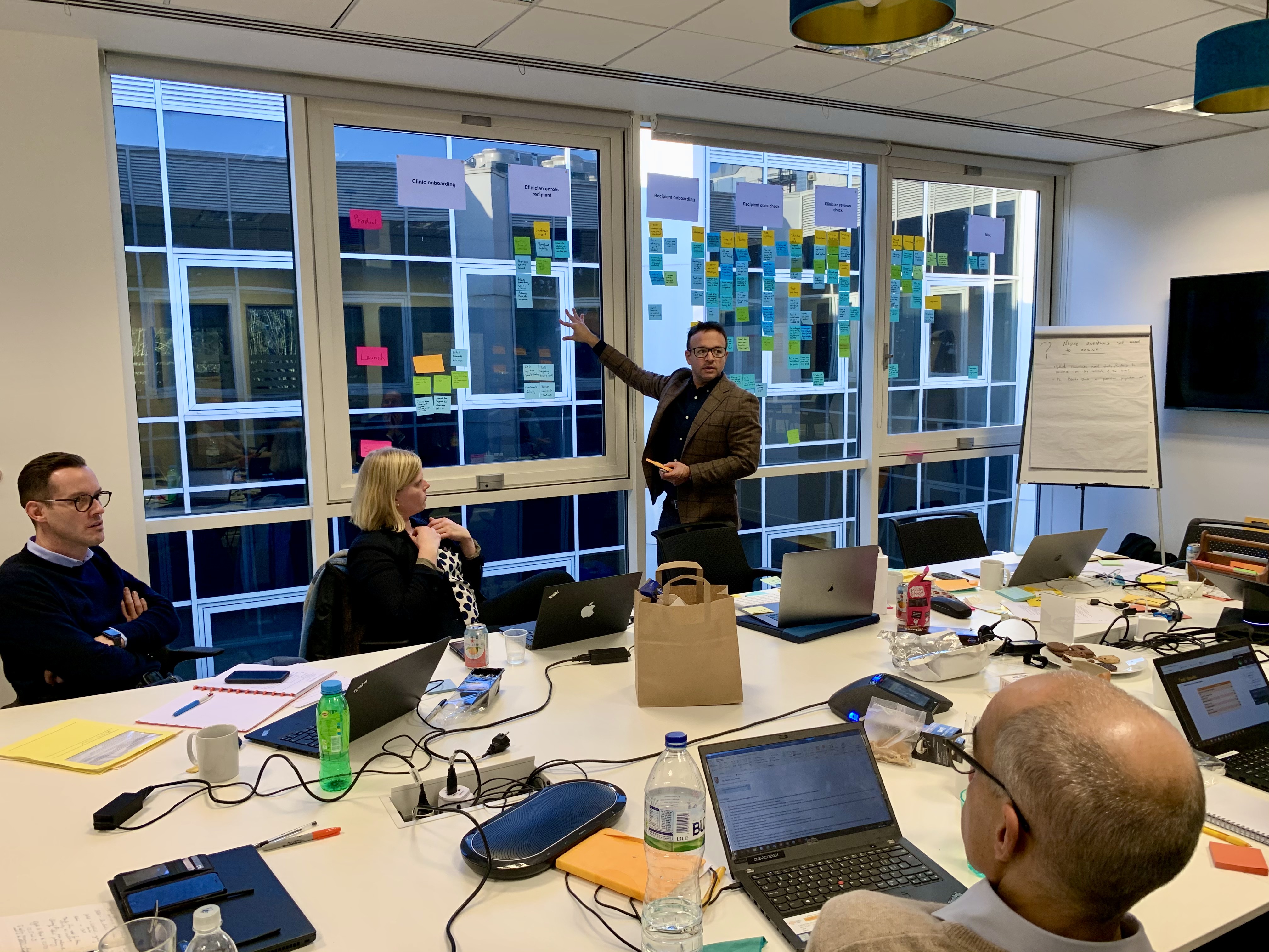 A presenter discussing workshop findings arranged across the windows with colleagues around a table.